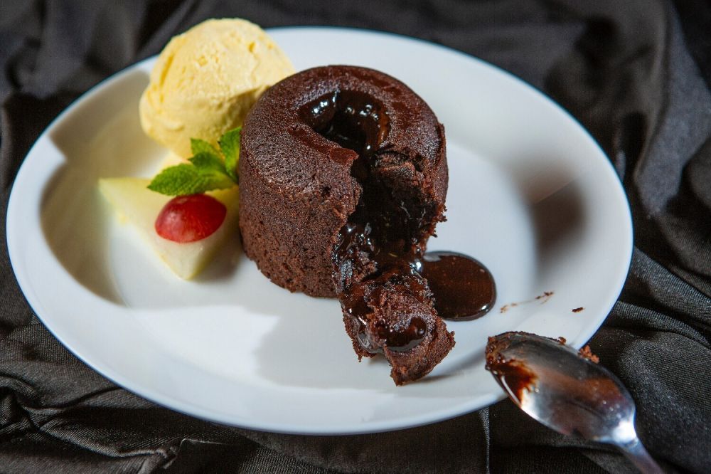 Sepotong cokelat hitam di atas meja kayu dengan biji kakao, pencahayaan hangat