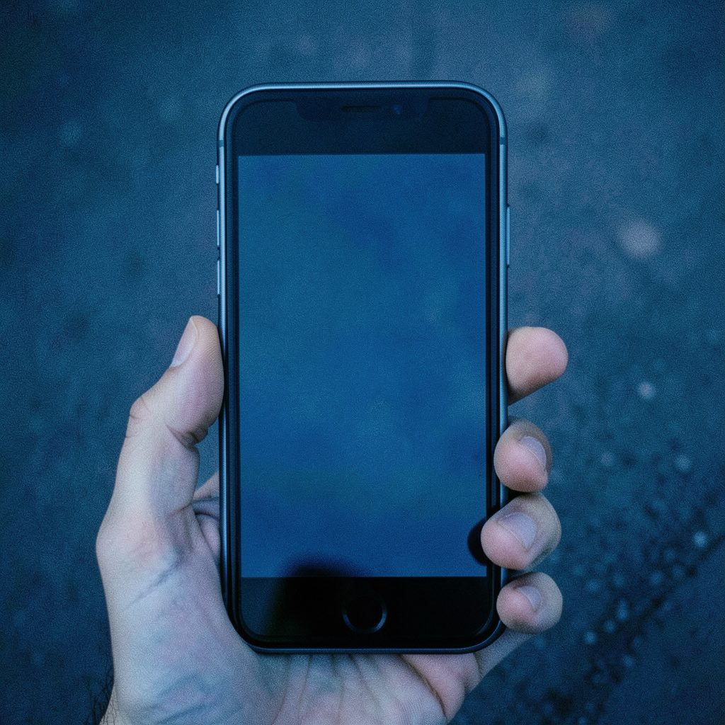 Smartphone modern dengan layar menyala menampilkan antarmuka aplikasi, latar belakang gelap